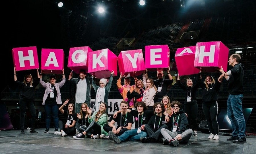 Grupa ludzi na scenie trzymająca różowe hasło HackYeah