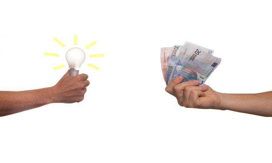 Zdjęcie przedstawia dwie dłonie, jedna trzyma żarówkę jako symbol pomysłu/idei, druga banknoty euro.